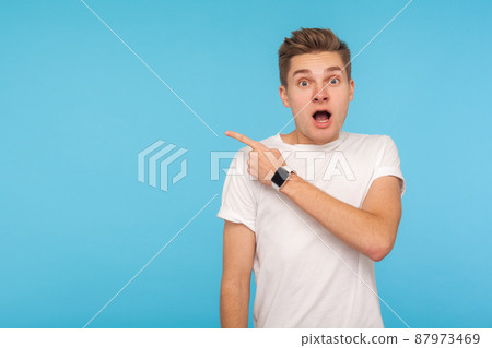 Wow look, advertise here. Portrait of young man expressing amazement and shock while pointing to the side, showing blank copy space for crazy idea presentation. studio shot isolated on blue background 87973469