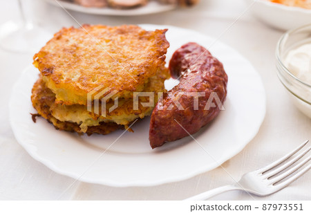 Potato pancakes with fried sausage on white plate Potato pancakes with fried sausage on white plate 87973551