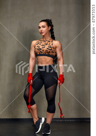 Attractive Young Woman Standing Strong In The Gym And Flexing Muscles - Beautiful Athletic Fitness Model Posing After Exercises. Attractive Young Woman Standing Strong In The Gym And Flexing Muscles - Beautiful Athletic Fitness Model Posing After Exercises. 87973553