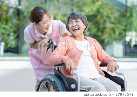 一位坐在輪椅上的高級婦女和一位推著輪椅的年輕女護士的畫像。 一位坐在輪椅上的高級婦女和一位推著輪椅的年輕女護士的畫像。 87973571