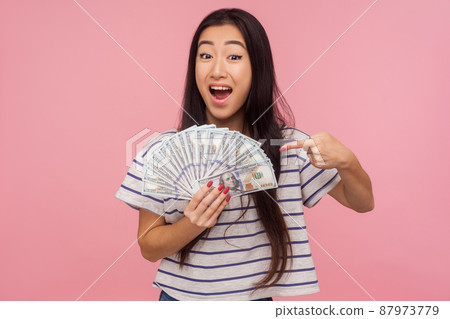 Wow, I'm rich. Portrait of shocked surprised girl with brunette hair pointing at dollar bills with amazed look, feeling wealthy successful, winning lottery. studio shot isolated on pink background Wow, I'm rich. Portrait of shocked surprised girl with brunette hair pointing at dollar bills with amazed look, feeling wealthy successful, winning lottery. studio shot isolated on pink background 87973779