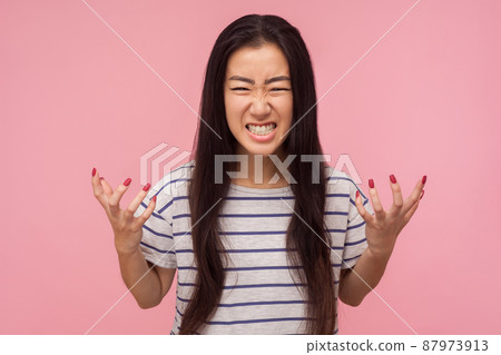 Portrait of enraged furious girl with long hair in striped t-shirt standing with clenched teeth and raised hands expressing wild anger, feeling crazy. indoor studio shot isolated on pink background 87973913