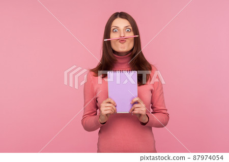 Funny young woman having fun holding pencil with lip and nose, female student resting during hometask doing. Indoor studio shot isolated on pink background 87974054