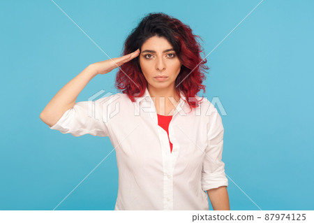 Yes sir. Portrait of responsible serious hipster woman with fancy red hair in white shirt saluting commander, listening order with obedient expression. indoor studio shot isolated on blue background 87974125