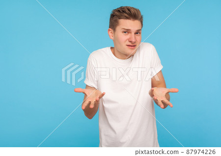 What do you want. Portrait of confused man in t-shirt expressing misunderstanding, gesturing in puzzlement with indignant face, asking why'd you do that. indoor studio shot isolated on blue background 87974226