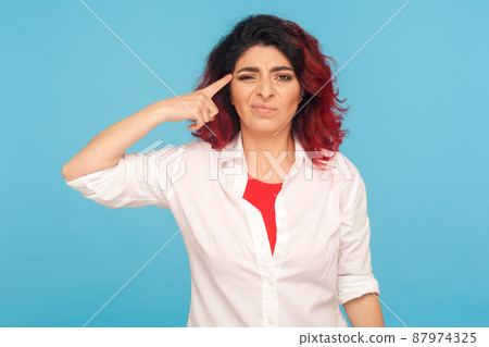 Bad idea. Portrait of disappointed unhappy woman in white shirt making stupid dumb cuckoo gesture with finger near head, dissatisfied with senseless talk. studio shot isolated on blue background Bad idea. Portrait of disappointed unhappy woman in white shirt making stupid dumb cuckoo gesture with finger near head, dissatisfied with senseless talk. studio shot isolated on blue background 87974325