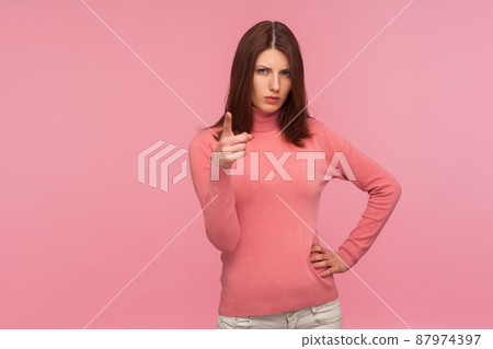 Hey you, be careful. Strict bossy woman with brown hair in pink sweater seriously pointing finger and looking at camera, warning. Indoor studio shot isolated on pink background Hey you, be careful. Strict bossy woman with brown hair in pink sweater seriously pointing finger and looking at camera, warning. Indoor studio shot isolated on pink background 87974397