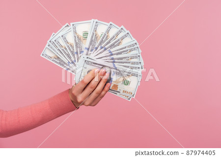 Closeup side view female hand in pink sweater holding and showing dollar banknotes, big salary, profit. Indoor studio shot isolated on pink background 87974405