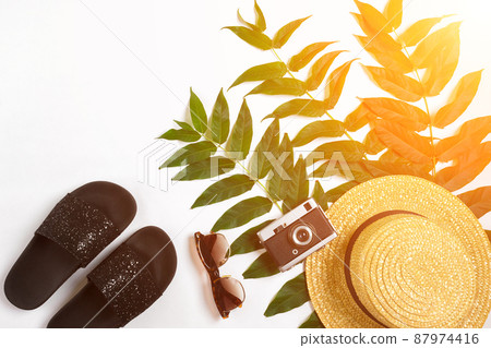 Straw hat with green leaves and old camera on white background, Summer background. Top view. Sun flare 87974416