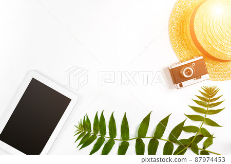 Straw hat with green leaves, tablet and old camera on white background, Summer background. Top view. Sun flare 87974453