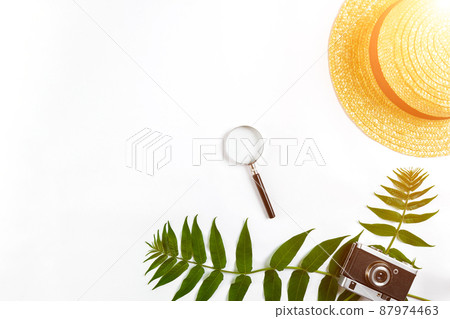 Straw hat with green leaves and old camera on white background, Summer background. Top view. Sun flare 87974463