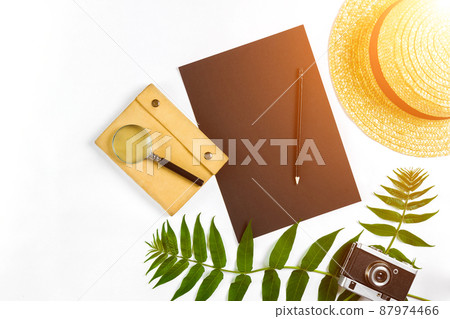 Straw hat with green leaves and old camera on white background, Summer background. Top view. Sun flare Straw hat with green leaves and old camera on white background, Summer background. Top view. Sun flare 87974466