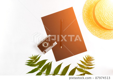 Straw hat with green leaves and old camera on white background, Summer background. Top view. Sun flare Straw hat with green leaves and old camera on white background, Summer background. Top view. Sun flare 87974513