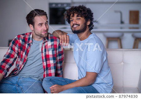 Romantic biracial gay couple sitting on the sofa Romantic biracial gay couple sitting on the sofa 87974830
