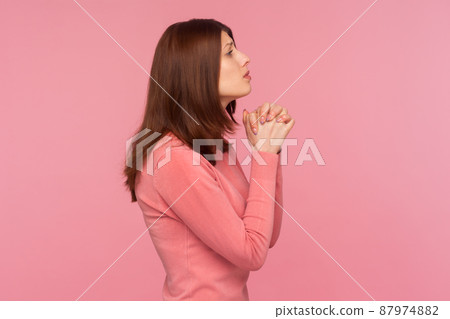 Profile portrait brunette woman in pink sweater praying god pressing hands, faith and religion. Indoor studio shot isolated on pink background 87974882