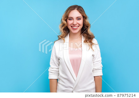 Portrait of vivid positive lovely bright businesswoman wearing casual white jacket looking at camera with perfect teeth smile, filled with joy optimism. indoor studio shot isolated on blue background 87975214