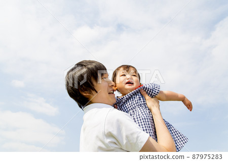 Looking up at a young father holding his little daughter against the blue sky from a low angle. Image of parent and child, family, father and child, childcare Looking up at a young father holding his little daughter against the blue sky from a low angle. Image of parent and child, family, father and child, childcare 87975283