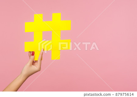 Closeup of hand holding large yellow paper hashtag symbol next to copy space, hash sign of famous media content, social media marketing and blog promotion. studio shot isolated on pink background Closeup of hand holding large yellow paper hashtag symbol next to copy space, hash sign of famous media content, social media marketing and blog promotion. studio shot isolated on pink background 87975614