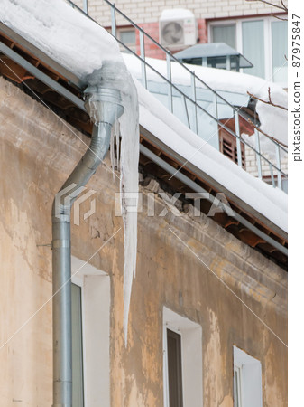 Ice icicles hang from a drainpipe at the edge of the roof. Ice icicles hang from a drainpipe at the edge of the roof. 87975847