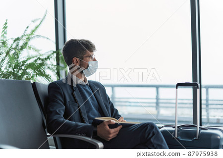 airport passenger in a protective mask taking notes in his notebook. airport passenger in a protective mask taking notes in his notebook. 87975938