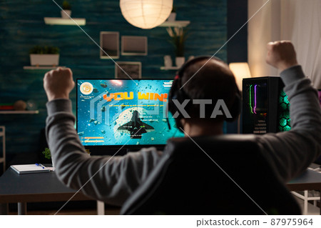 Man raising hands after winning video games on computer. Person playing online games with monitor and headphones, celebrating win and feeling happy. Player with gaming technology Man raising hands after winning video games on computer. Person playing online games with monitor and headphones, celebrating win and feeling happy. Player with gaming technology 87975964