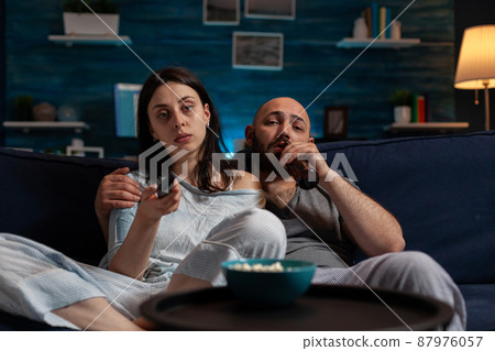 POV of woman and man switching channels with TV remote control, finding fun movie to watch for entertainment. Girlfriend and boyfriend doing film selection to relax with leisure activity. 87976057