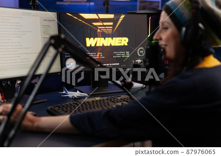 Woman live streaming online video games on computer. Person broadcasting gameplay, playing live on stream with chat, using monitor and microphone. Streamer wearing headphones to play. Woman live streaming online video games on computer. Person broadcasting gameplay, playing live on stream with chat, using monitor and microphone. Streamer wearing headphones to play. 87976065