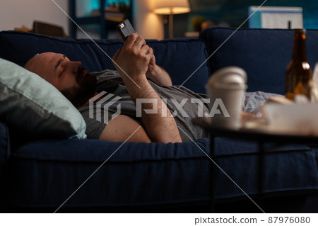 Bored sad person with chronic depression using smartphone to browse internet and text on social media. Anxious lonely man suffering from mental health illness, having mobile phone. Bored sad person with chronic depression using smartphone to browse internet and text on social media. Anxious lonely man suffering from mental health illness, having mobile phone. 87976080