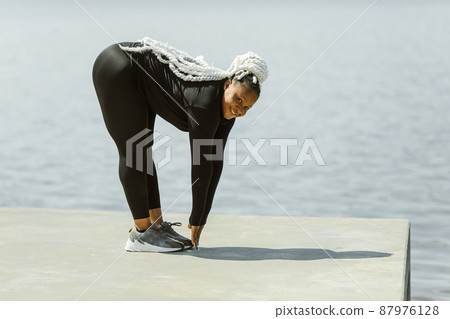 Afro-american plus size woman doing yoga outdoor near the lake 87976128