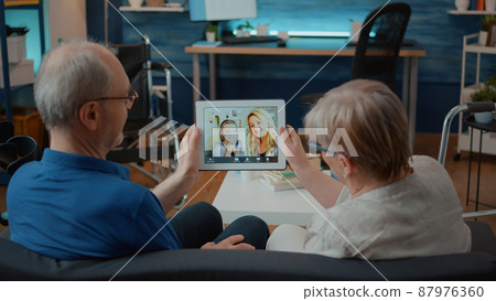 Senior husband and wife waving at video call webcam to chat with relatives on digital tablet. Elder people with physical disability using online videoconference to start remote discussion. Senior husband and wife waving at video call webcam to chat with relatives on digital tablet. Elder people with physical disability using online videoconference to start remote discussion. 87976360