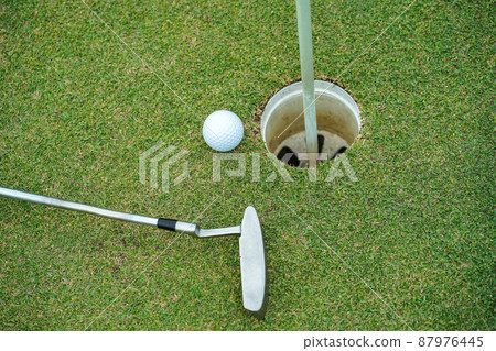 Top view of a golf ball with putter on green course at hole. Top view of a golf ball with putter on green course at hole. 87976445