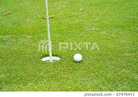 Top view of a golf ball on green course at hole. Golf ball and golf club on green in the evening golf course with sunshine. 87976451