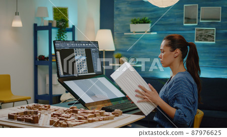 Architect looking at computer with building model for construction layout project. Woman engineer working with maquette and blueprint plan for graphic development work in office. 87976625
