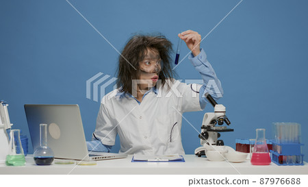 Amusing crazy chemist analyzing liquid in test tube at desk, doing insane mad facial expressions with dirty face and messy wacky hair. Foolish goofy woman being silly and funny on camera. Amusing crazy chemist analyzing liquid in test tube at desk, doing insane mad facial expressions with dirty face and messy wacky hair. Foolish goofy woman being silly and funny on camera. 87976688