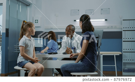 Physician greeting little girl and mother in medical cabinet. Male doctor and patient having conversation about disease and prescription treatment at annual checkup visit. Health service 87976972