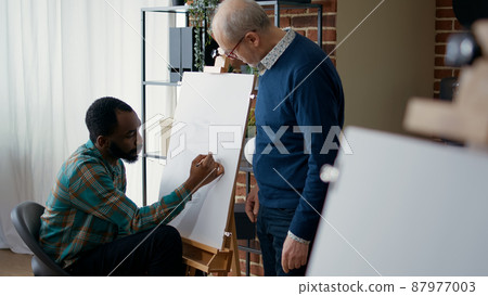 Elder artist teaching art class student new drawing technique to help with educational development and growth. Creative person receiving artistic advice from senior man to draw masterpiece. 87977003
