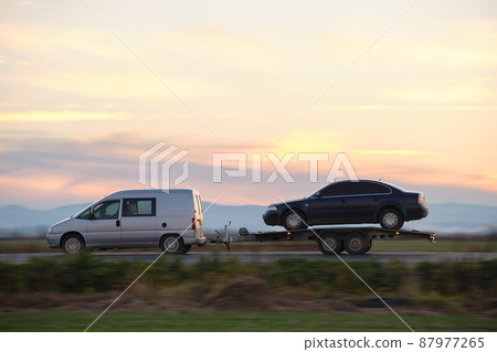 Tow truck vehicle with car transporting carrier trailer driving on highway in evening Tow truck vehicle with car transporting carrier trailer driving on highway in evening 87977265