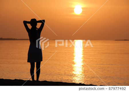 Lonely young woman standing on ocean beach by seaside enjoying warm tropical evening. Lonely young woman standing on ocean beach by seaside enjoying warm tropical evening. 87977492
