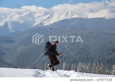 Hiker with backpack walking on snowy mountain hillside on cold winter day. 87977538