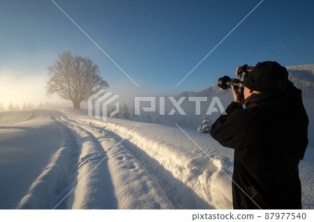 Hiker photographer taking pictures of snowy nature in winter mountains. 87977540
