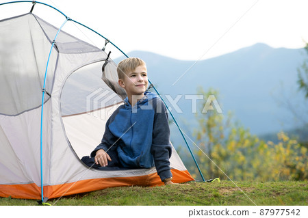 Hiker child boy resting in a tourist tent at mountain campsite enjoying view of beautiful summer nature. Hiker child boy resting in a tourist tent at mountain campsite enjoying view of beautiful summer nature. 87977542
