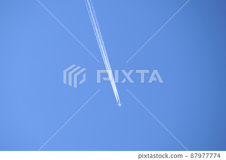 Distant passenger jet plane flying on high altitude on clear blue sky leaving white smoke trace of contrail behind. Air transportation concept. 87977774