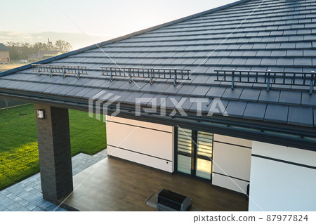 Closeup snow guard for safety in winter on house roof top covered with ceramic shingles. Tiled covering of building 87977824
