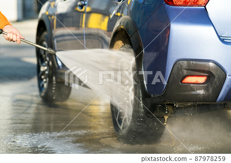 Closeup of male driver washing his car with contactless high pressure water jet in self service car wash. Closeup of male driver washing his car with contactless high pressure water jet in self service car wash. 87978259