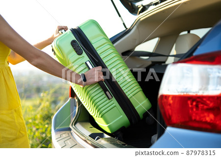 Close up of woman hands taking green suitcase from car trunk. Travel and vacations concept. 87978315