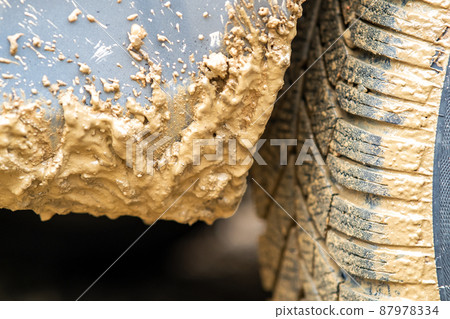 Close up of dirty car wheel with rubber tire covered with yellow mud. 87978334