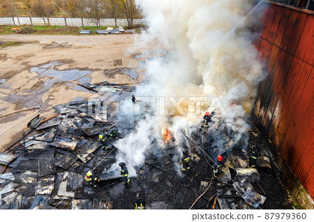Aerial view of firefighters extinguishing fire in industrial area. Aerial view of firefighters extinguishing fire in industrial area. 87979360