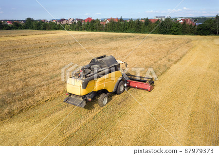 Aerial view of combine harvester harvesting large ripe wheat field. Agriculture from drone view. Aerial view of combine harvester harvesting large ripe wheat field. Agriculture from drone view. 87979373