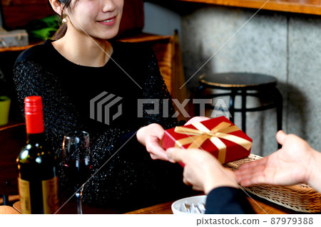 A young Asian woman giving a present to a man at a restaurant A young Asian woman giving a present to a man at a restaurant 87979388