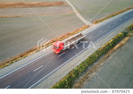 Aerial view of blurred fast moving semi-truck with cargo trailer driving on highway hauling goods in evening. Delivery transportation and logistics concept 87979425